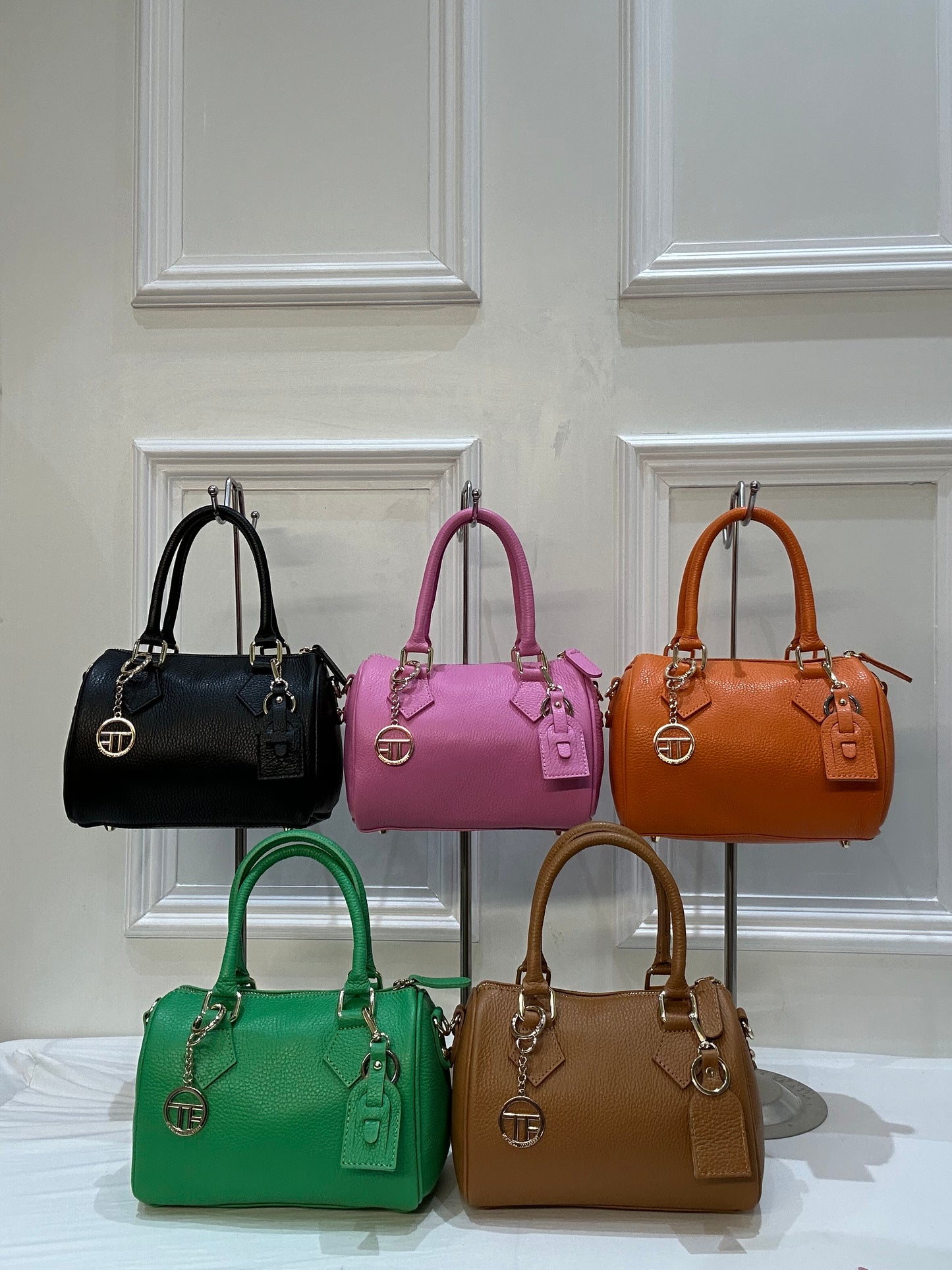 Five small leather tote bags in black, pink, orange, green, and brown displayed on a stand.