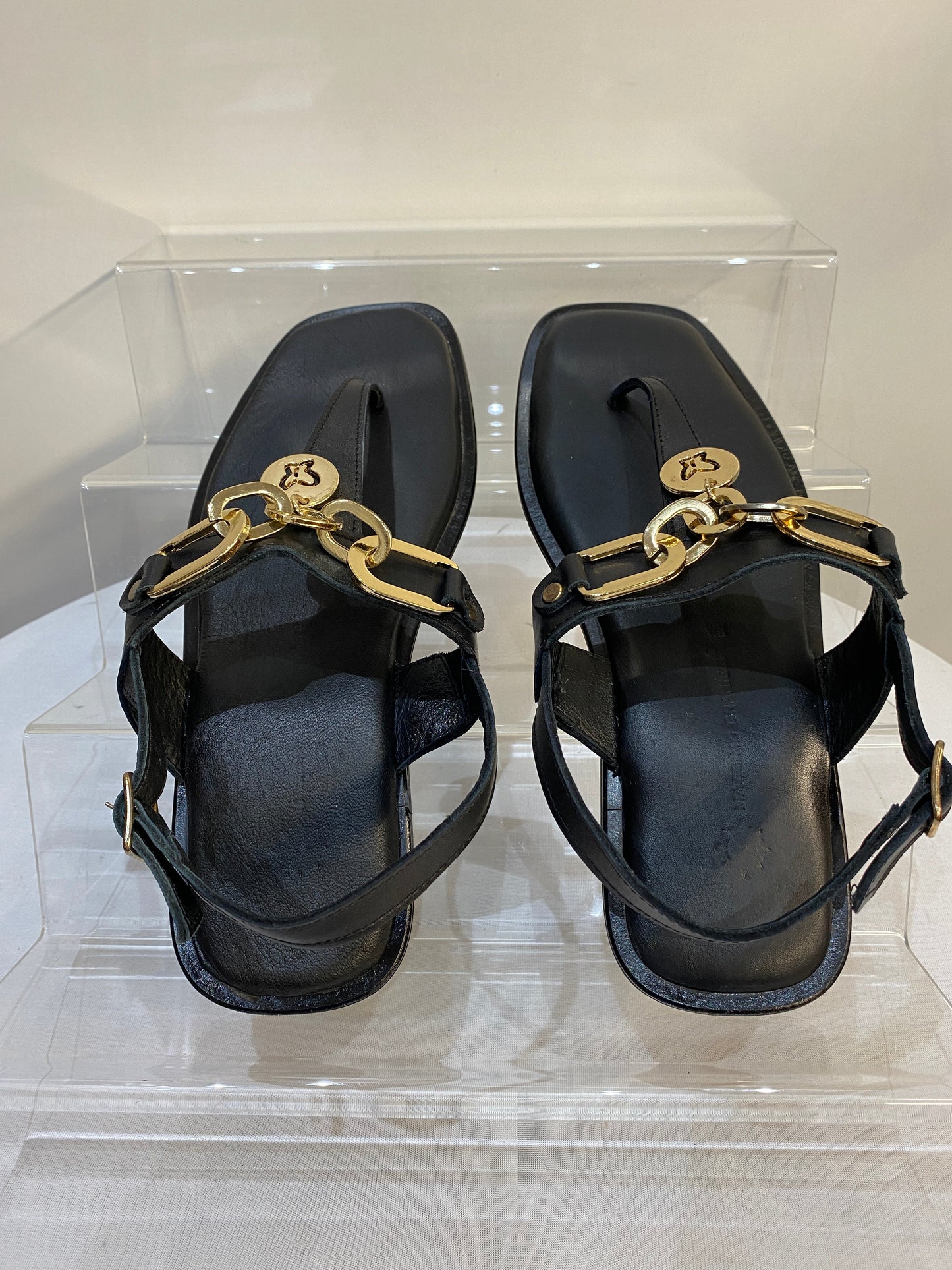 Black leather thong chain flat sandals with gold chain detailing and adjustable ankle strap.